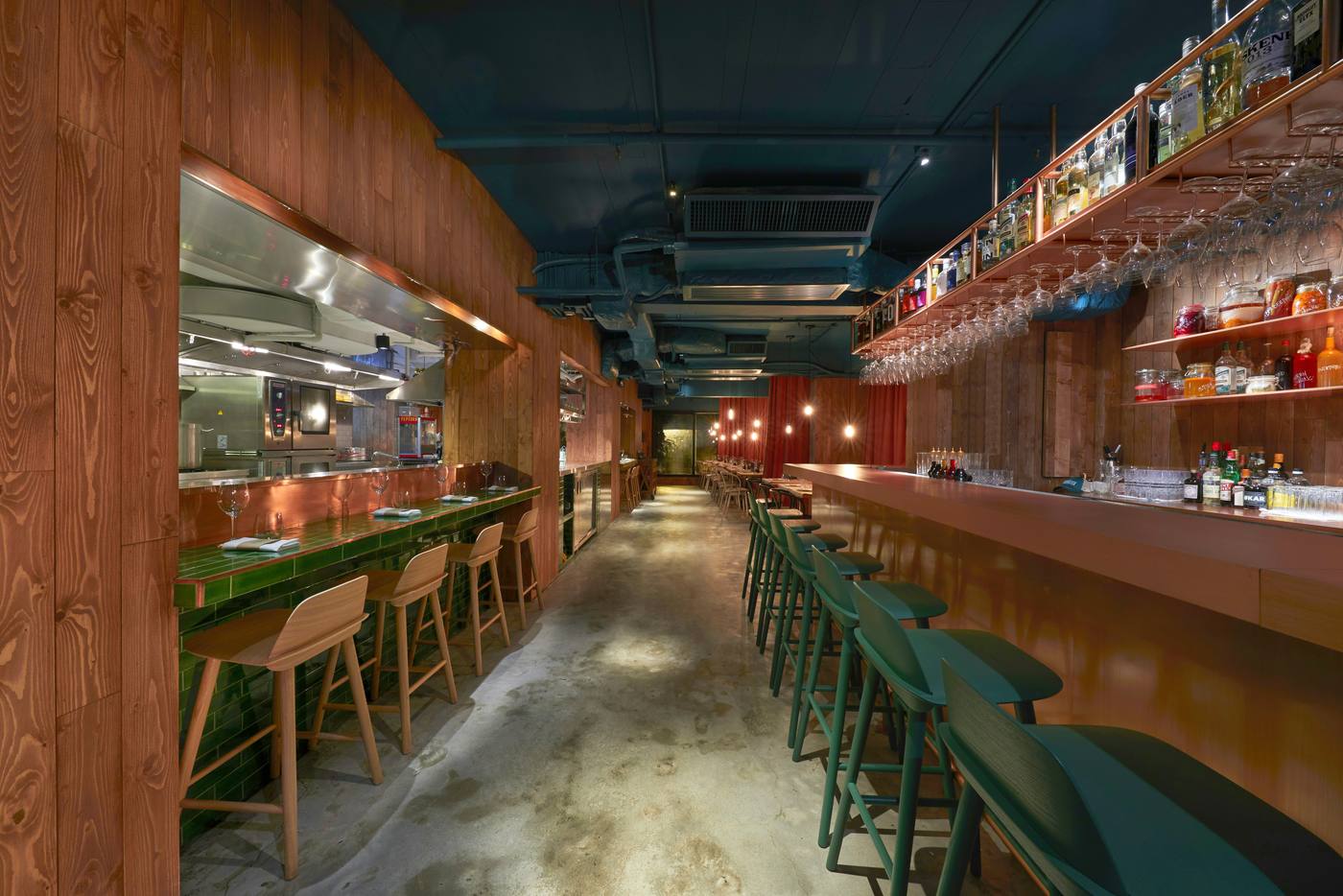 Empty restaurant bar with green stools, a wood bar top and an open kitchen pass